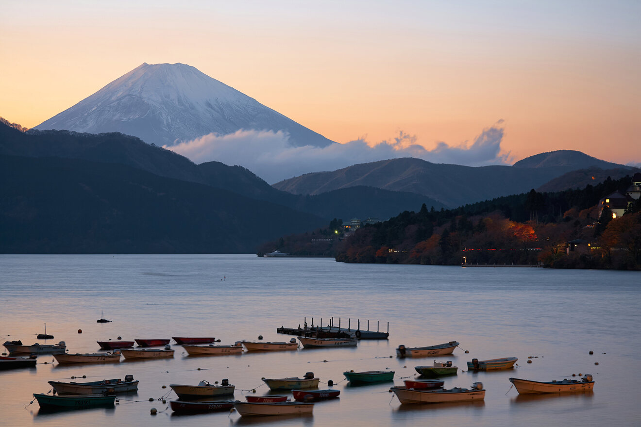 Twilight view of Mount Fuji towering over a peaceful lake dotted with small boats and a hint of the day's last light on the horizon